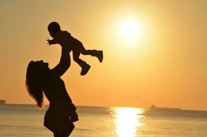 Silhouette of an adult lifting a child towards the golden sunset over the ocean.