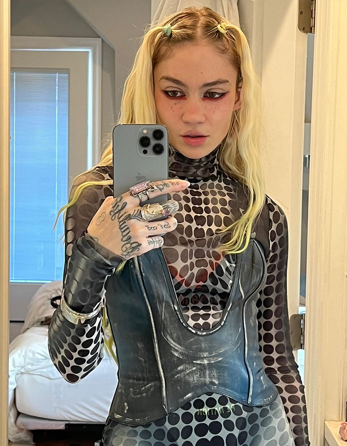 Musician Grimes takes a mirror selfie, wearing a patterned outfit, amid controversy.