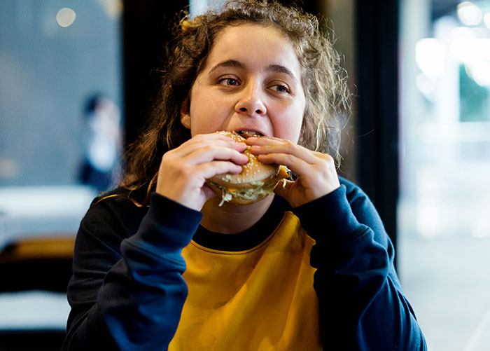 A person in a casual setting enjoying a burger, highlighting the ordinary experiences of wealthy people.