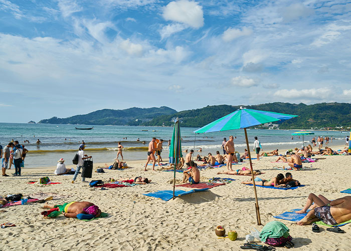 People on a busy beach with umbrellas and towels, enjoying a sunny day by the sea.