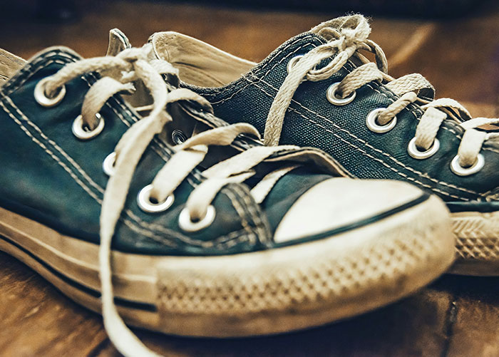 Worn black sneakers with white laces on a wooden floor, illustrating ordinary items among wealthy people's bizarre perceptions.