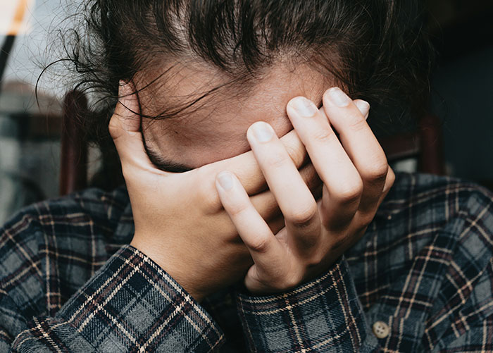 Person in a plaid shirt with face in hands, symbolizing surprise or disbelief about ordinary things in wealthy lives.