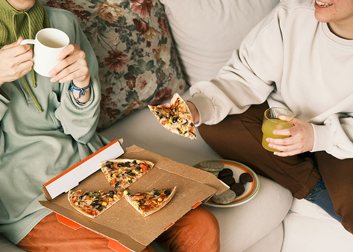 Wealthy people enjoying pizza and drinks on a couch, surrounded by snacks.