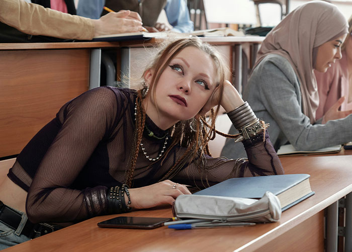 Student in a classroom, resting head on hand, appearing thoughtful. Wealthy experiences considered ordinary.