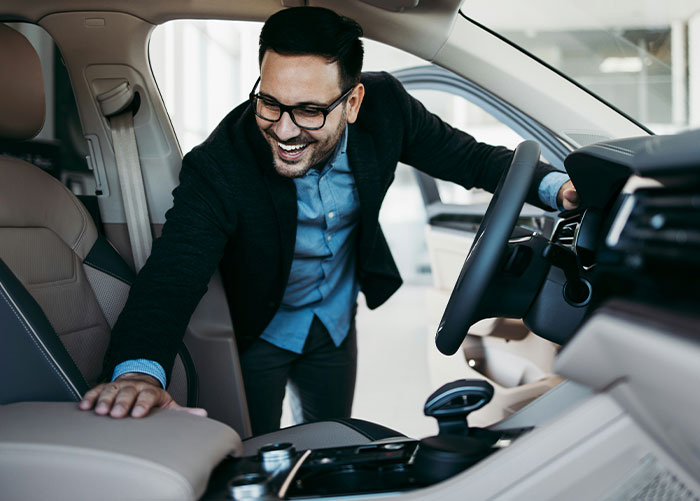 A man in a suit smiles while inspecting the interior of a luxury car, representing wealthy people's perspective on ordinary things.