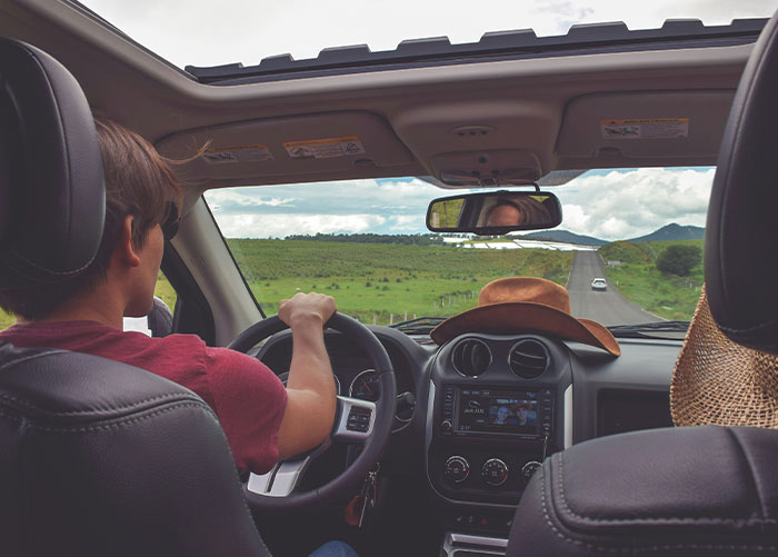 Wealthy person driving a car with a scenic view ahead, seen through a sunroof.