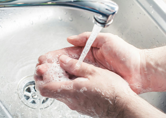 Washing hands under a running faucet, representing ordinary hygiene habits perceived as unusual by wealthy people.