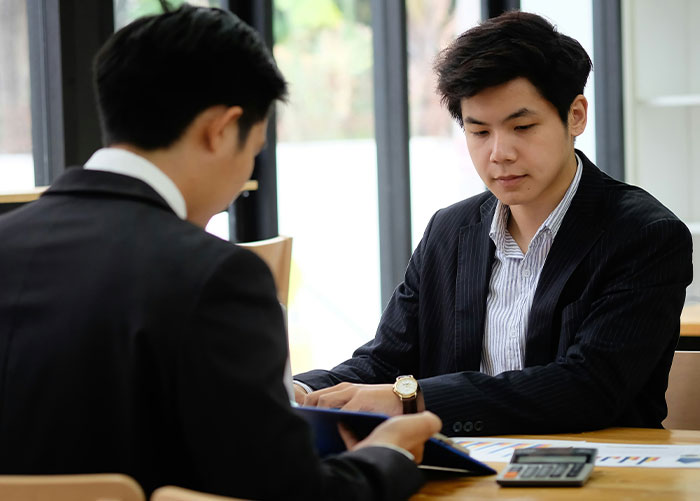 Two people in suits discussing documents at a table, reflecting wealth and ordinary business activities.