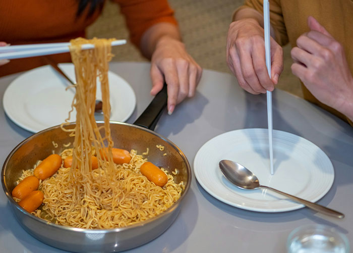 Wealthy individuals using chopsticks to eat instant noodles with sausages in a casual setting.