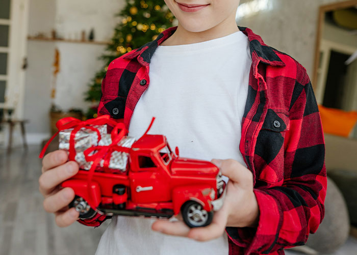 A child holding a toy red truck with gifts, wearing a red plaid shirt, representing wealth perspectives in a festive setting.