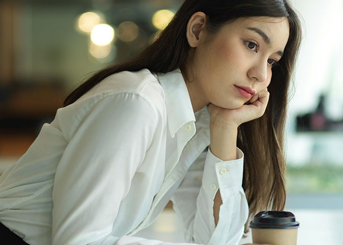 Woman in white shirt sitting thoughtfully with a coffee cup, representing wealthy people's perceptions.