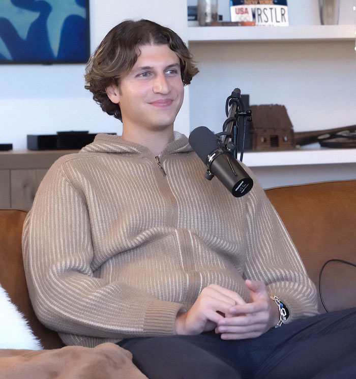 Man sitting on a couch with a microphone, discussing billionaire parodies online.