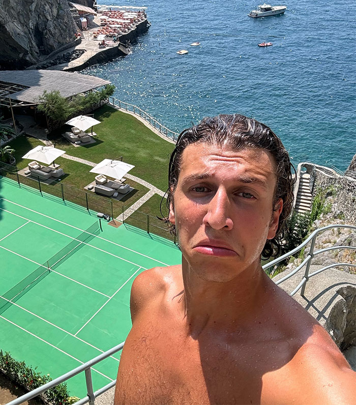 Man near cliffside tennis court with an ocean view, embodying a parody of luxury lifestyle online.