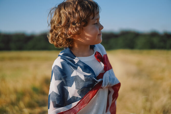 Child wrapped in a USA flag standing in a field, representing kids in a foreign country.