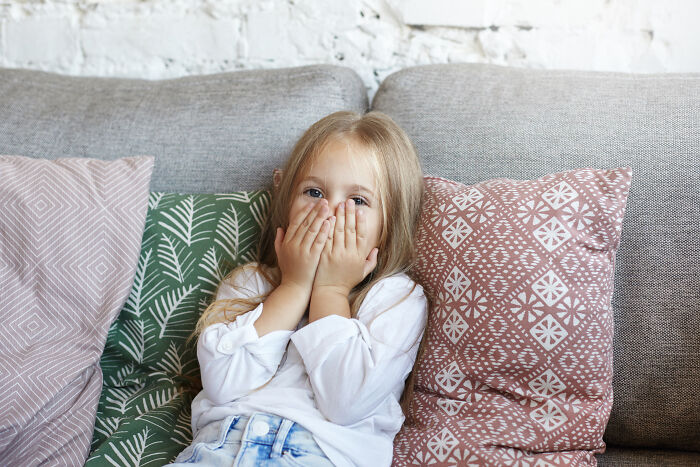 Young girl on a sofa covering her mouth, illustrating effects of a horrible parent.