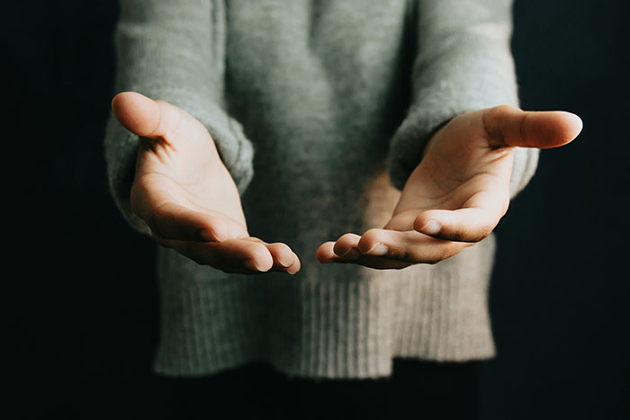 Outstretched hands wearing a gray sweater, symbolizing life lessons learned too late.