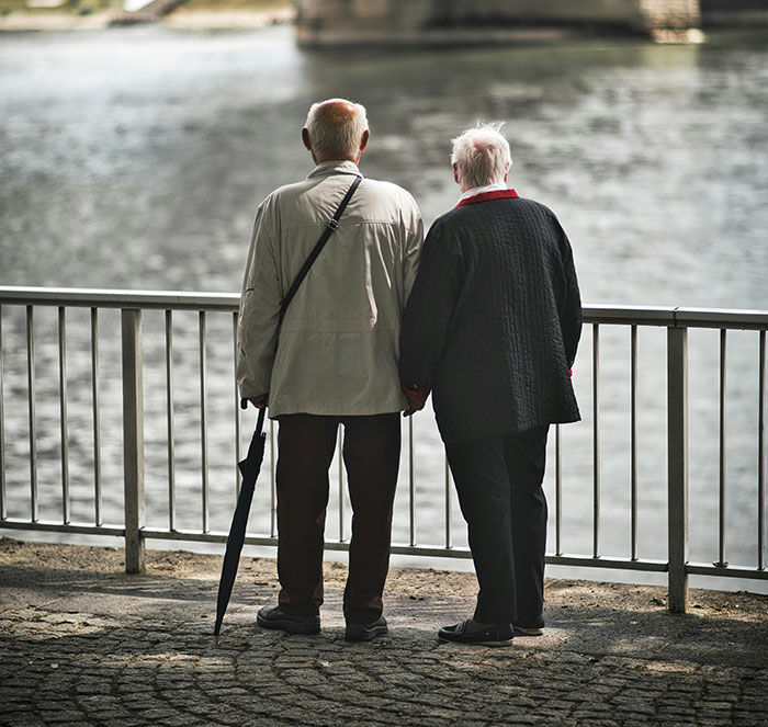 Two elderly people holding hands by a lakeside, symbolizing life lessons and reflections.