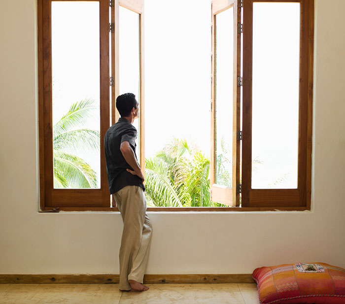 Man looking out window, contemplating life lessons with a view of palm trees.