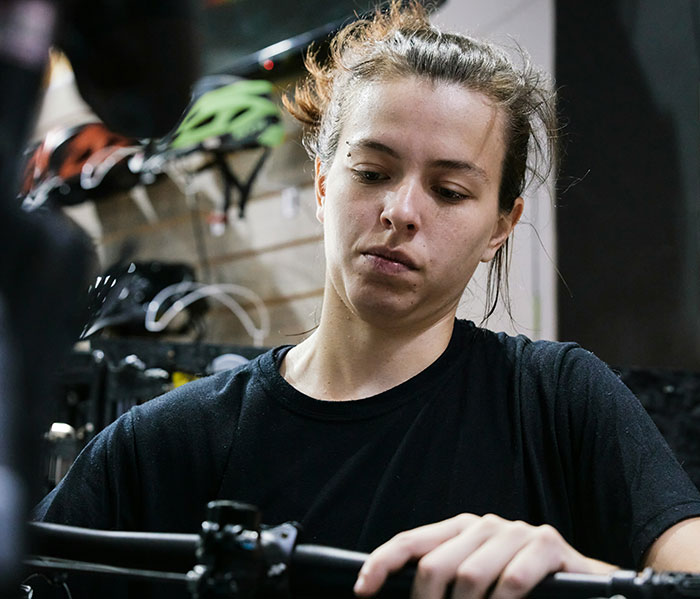 Young woman in a bike shop, concentrating on a task, reflecting on life lessons learned.