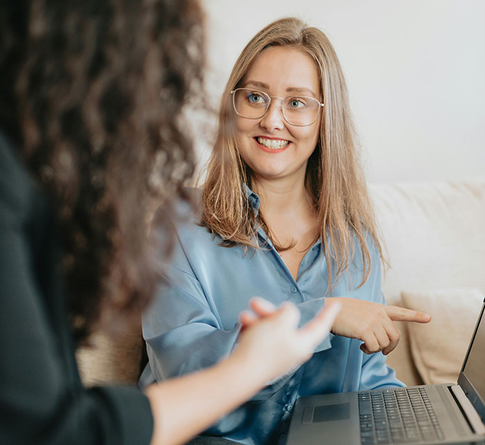 Woman in glasses smiling and pointing at a laptop, discussing life lessons in an informal setting.