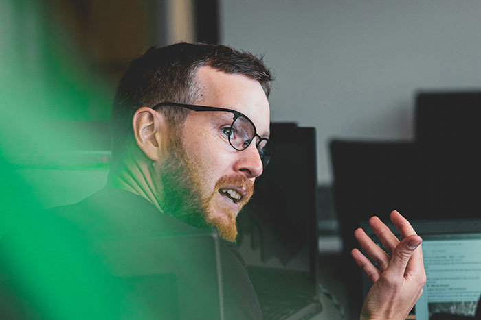 A man with glasses speaking passionately in an office environment, possibly sharing life lessons or insights.