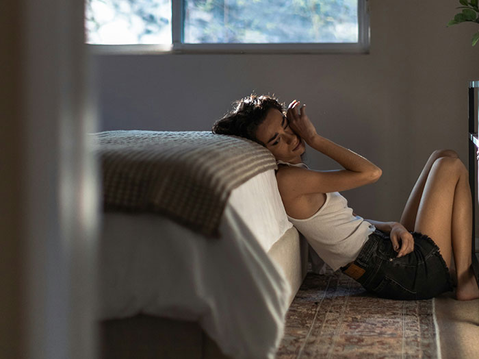 Person sitting on the floor by a bed, looking contemplative, illustrating life lessons and reflections.