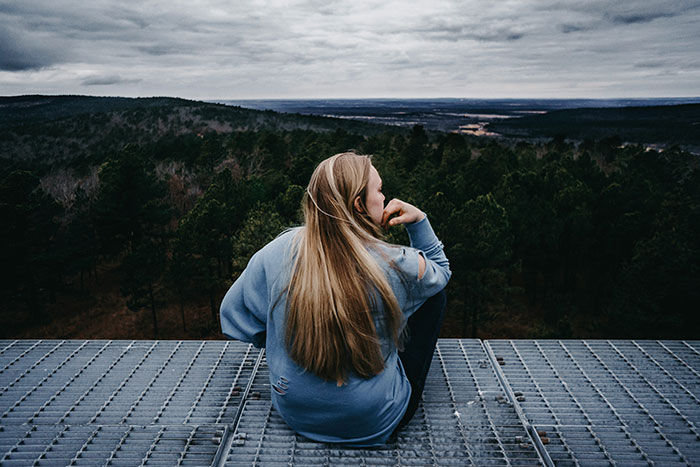 Person sitting on a platform overlooking a forest, reflecting on life lessons.