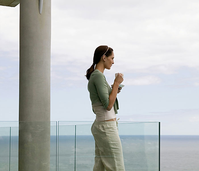 Woman in a green cardigan reflecting on life lessons, standing on a balcony overlooking the ocean.