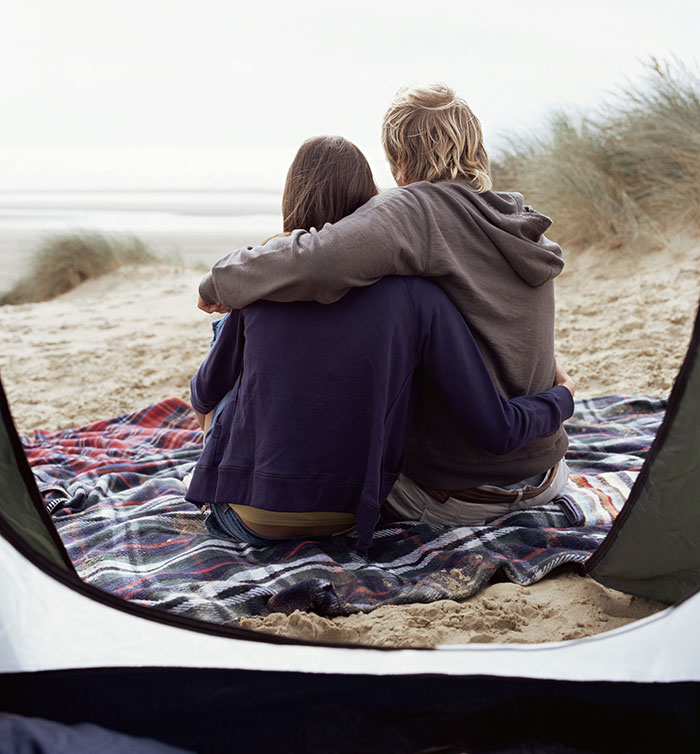 Couple sitting on a beach blanket, embracing, possibly reflecting on life lessons learned too late.