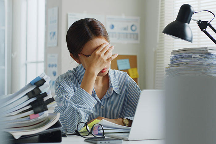 A stressed woman at a cluttered desk, realizing life lessons with papers and laptop in an office setting.