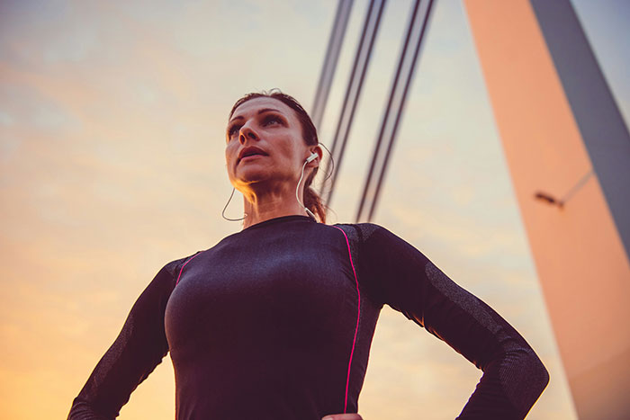 Woman with earbuds standing outdoors, contemplating life lessons at sunset.