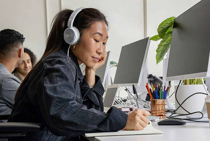 Woman wearing headphones, taking notes at her desk; reflecting on life lessons.