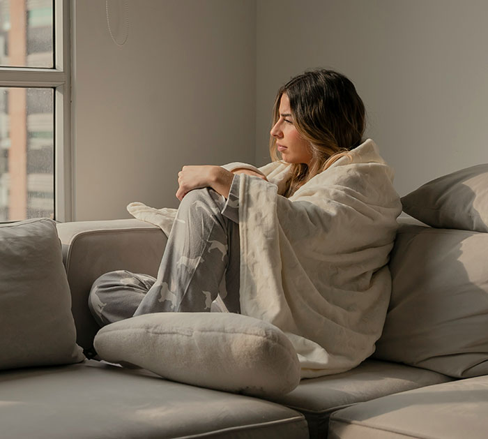 Woman in a cozy robe sits on a sofa, reflecting on life lessons and looking out the window.