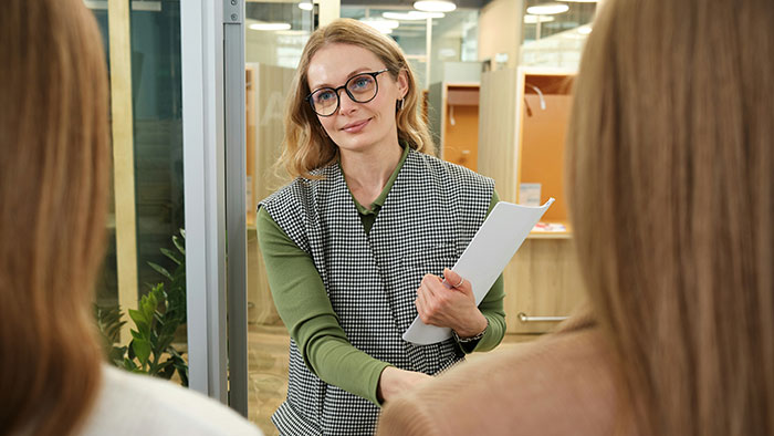 A woman in glasses holding documents, engaging in a conversation, representing life lessons learned too late.