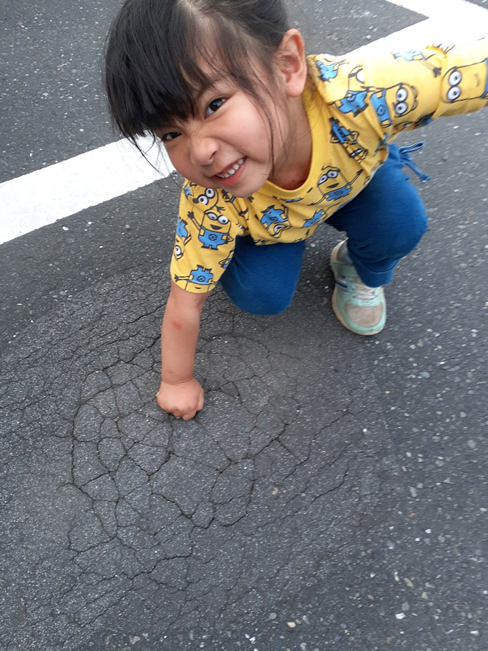 A child playfully pretends to punch through cracked pavement, creating a hilarious-kids moment.