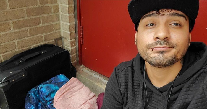 Man sitting by luggage, wearing a cap, representing journey from homelessness to surgical assistant.