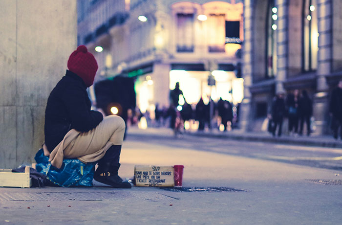 Homeless man sitting on a city street with a sign, illustrating search for change and new beginnings.