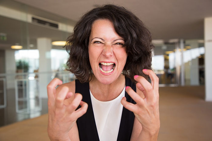 A woman in an office expressing frustration with clenched hands and open mouth.