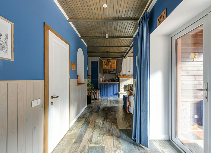 Bright interior hallway with blue walls and wooden flooring, leading to a cozy kitchen space.