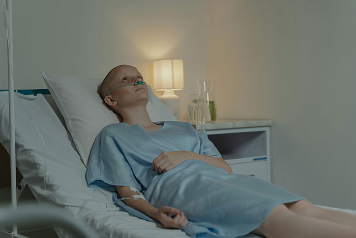 Woman in hospital bed, looking contemplative, illuminated by bedside lamp.