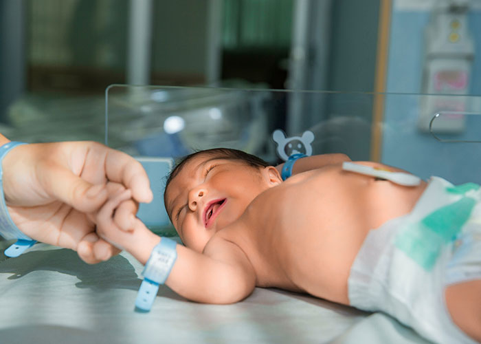 Newborn baby in a hospital bassinet gripping an adult's finger, highlighting normal yet profound life moments.