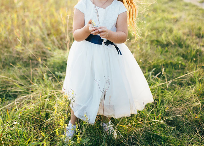 Child in white dress standing in a grassy field, representing normal things that may seem horrific on reflection.