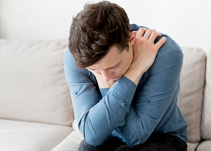 A person sitting on a couch, looking down with arms crossed, reflecting on normal things with a serious expression.