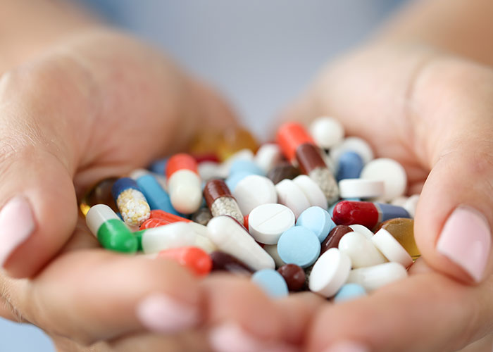 Hands holding a pile of colorful pills, illustrating the normal but potentially horrific reliance on medication.