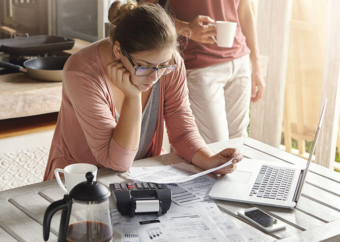 Person overwhelmed with paperwork at kitchen table, illustrating normal but potentially horrific daily tasks.