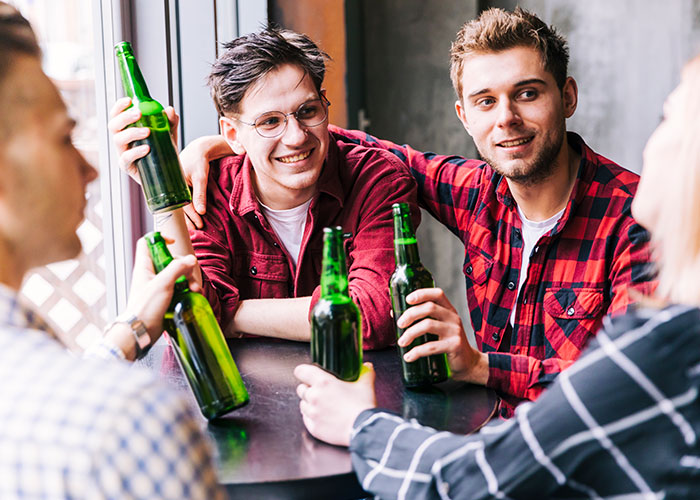 Friends enjoying drinks together, smiling and chatting while holding beer bottles in a lively social setting.