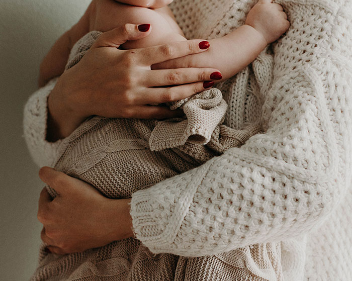 Person in a cozy sweater hugging a baby wrapped in a knit blanket, symbolizing a normal yet profound moment.