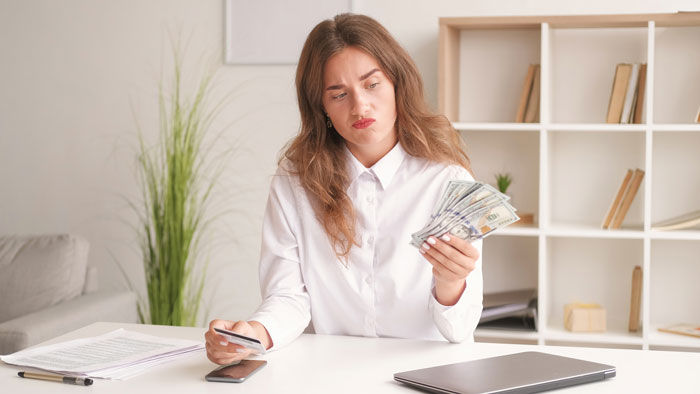 Woman at desk holding cash, concerned about hospital expenses for sister\'s childbirth.