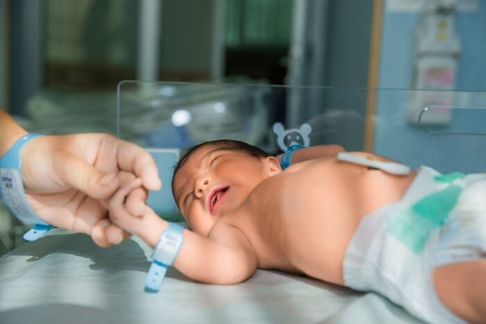 Newborn baby in a hospital nursery, wearing ID bands, lying on a bed, illustrating hospital bills for newborn care.