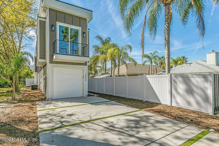 Small modern house with a garage in a Florida neighborhood, surrounded by palm trees.